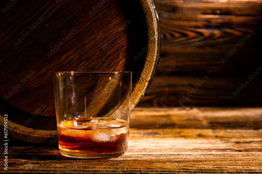 Glass of cold rum and barrel on wooden background