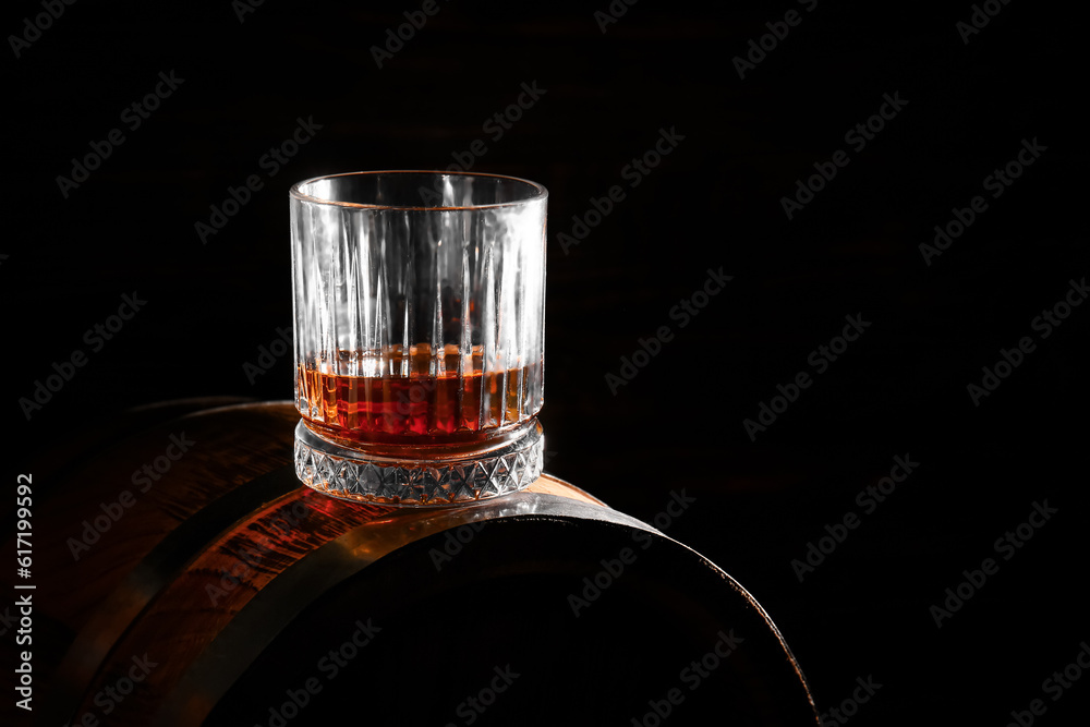 Barrel with glass of rum on black background