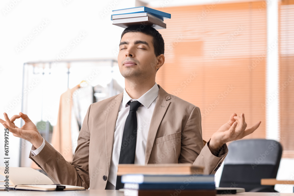 Young businessman with books meditating in office. Balance concept