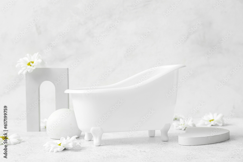 Small bathtub, chamomile flowers and decor on light background