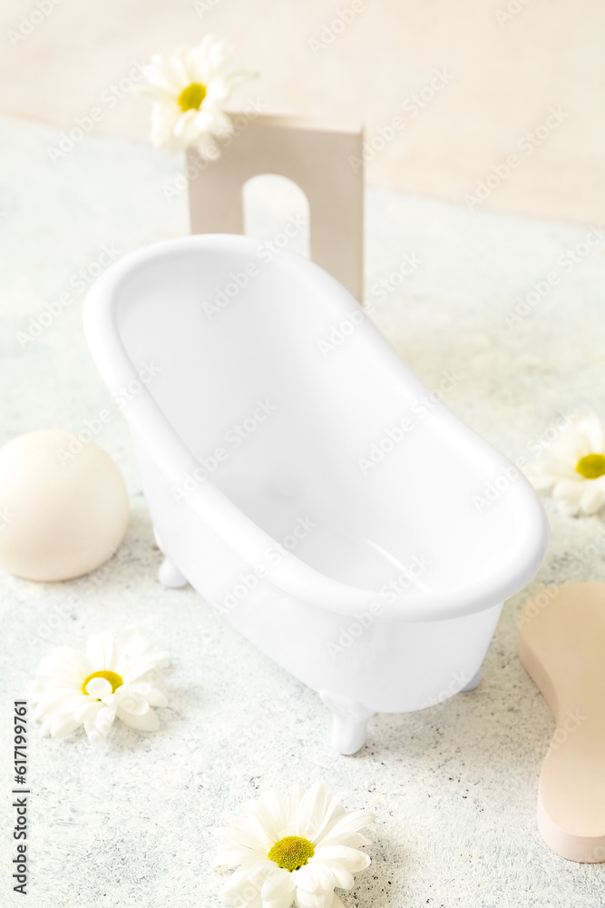 Small bathtub, chamomile flowers and decor on light background