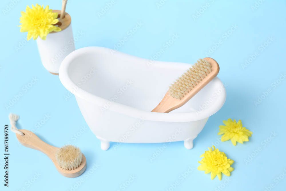 Small bathtub , massage brushes and flowers on color background