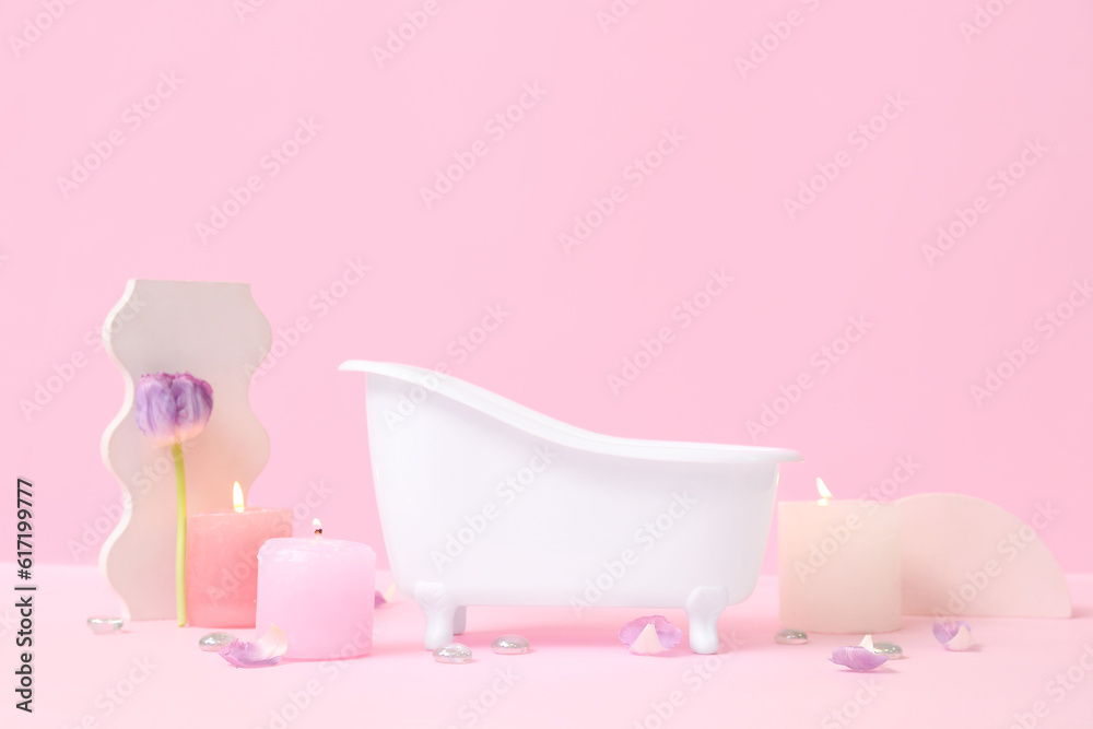 Small bathtub, burning candles and decor on pink background