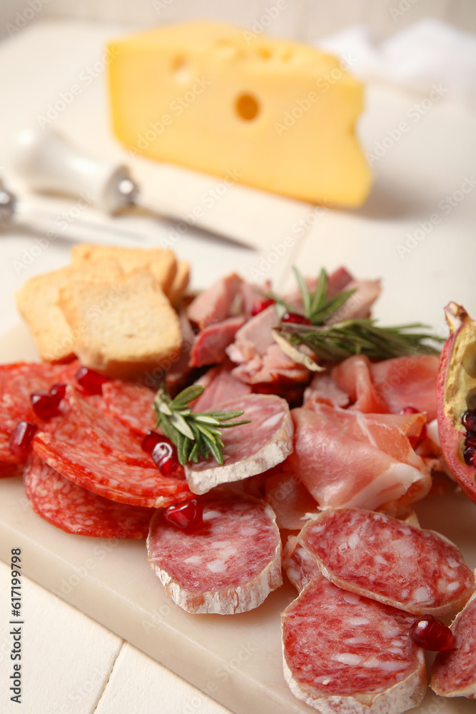 Board with assortment of tasty deli meats on white wooden background, closeup