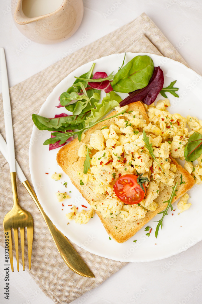 Plate with tasty scrambled eggs sandwich and salad on light background