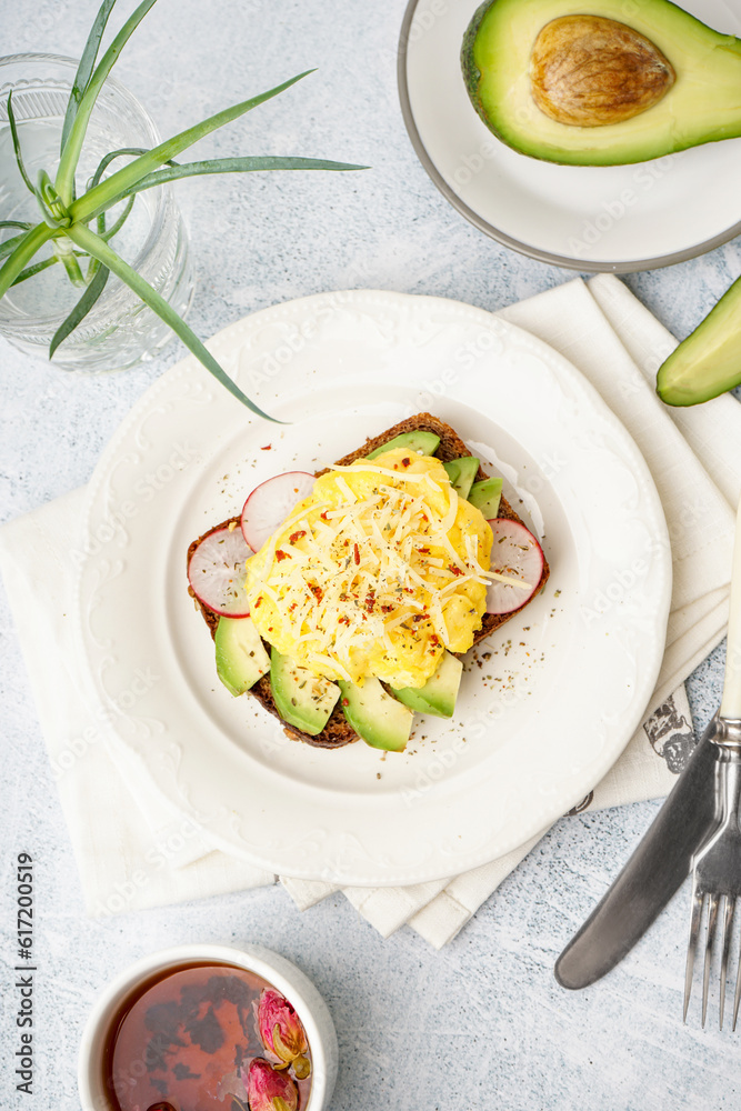 Plate with tasty scrambled eggs sandwich and vegetables on light background