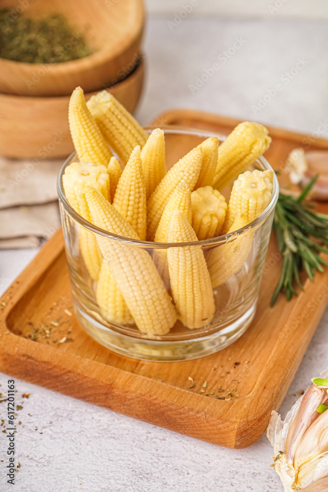 Glass with tasty canned corn cobs on light background