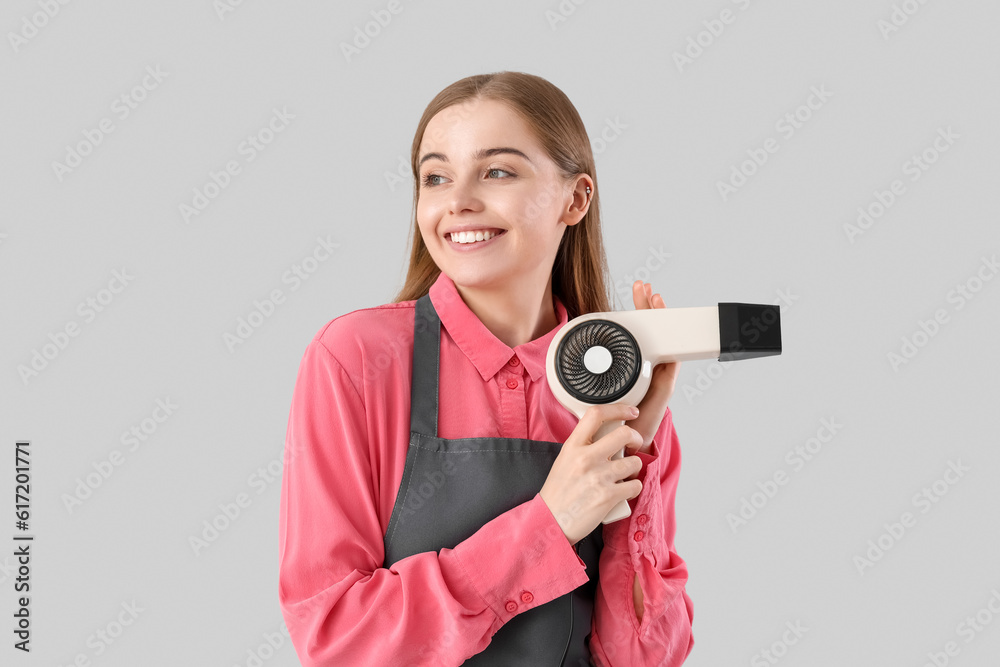 Female hairdresser with dryer on grey background