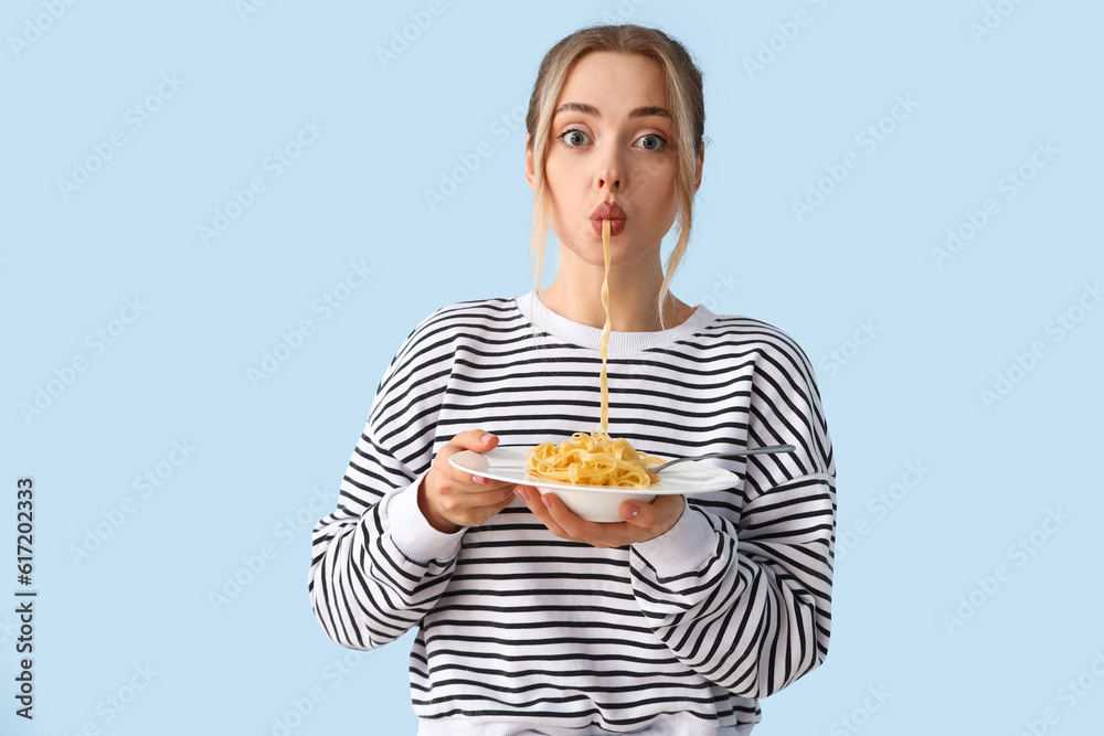 Young woman eating tasty pasta on blue background