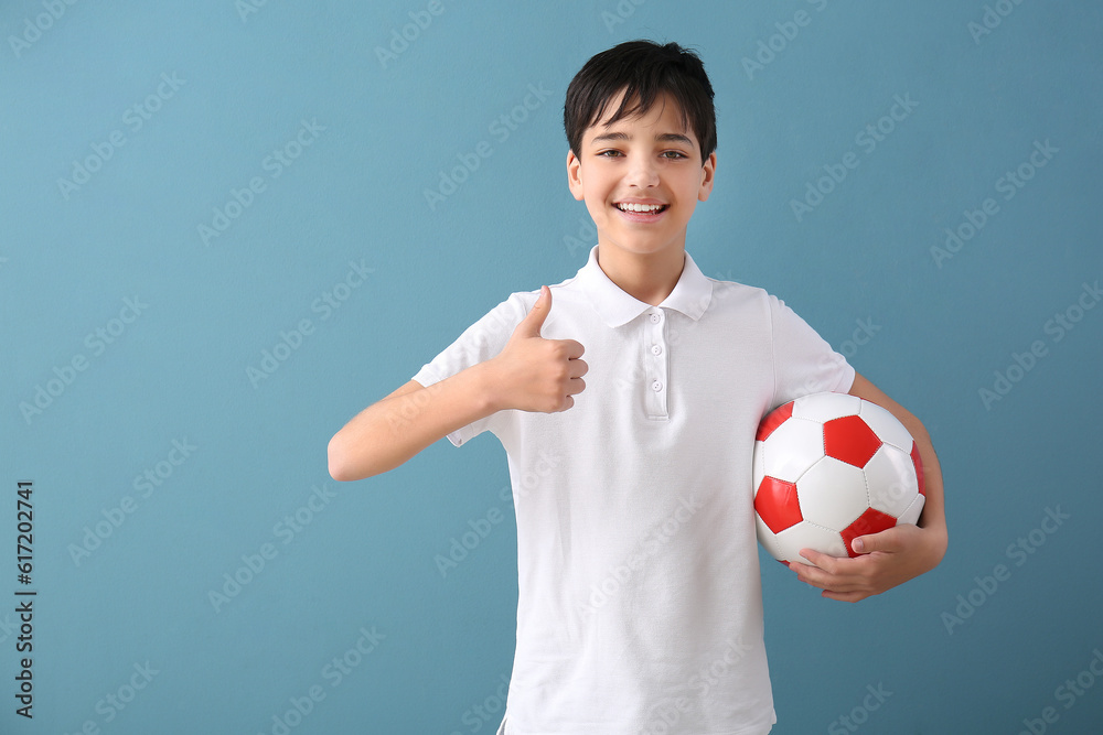 Little boy with soccer ball showing thumb-up on blue background