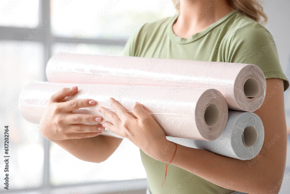 Young woman with wallpaper rolls at home, closeup