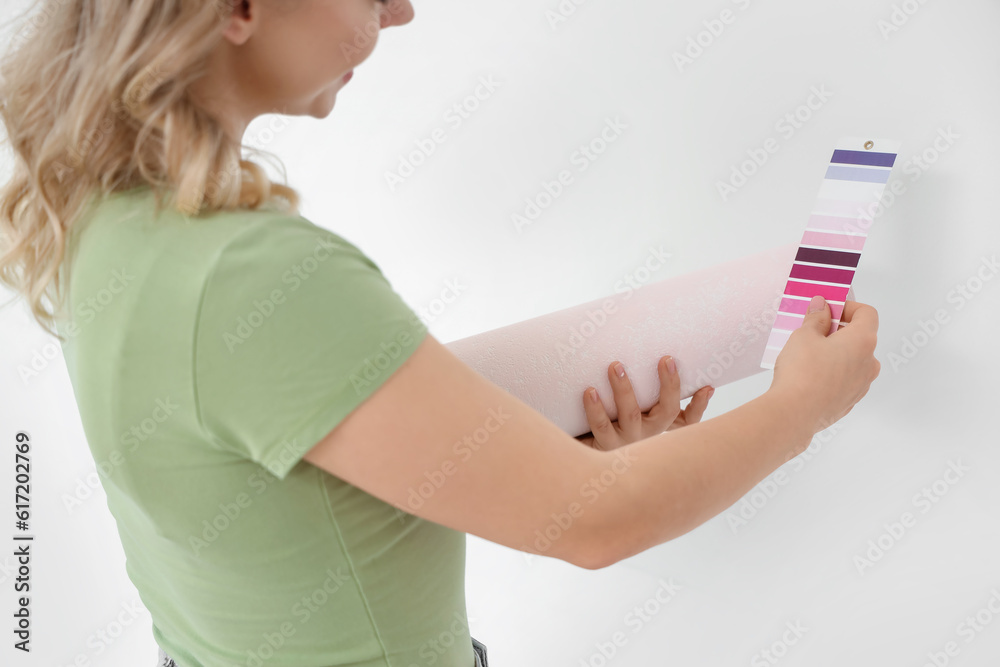 Young woman with wallpaper roll and paint color palette at home, closeup