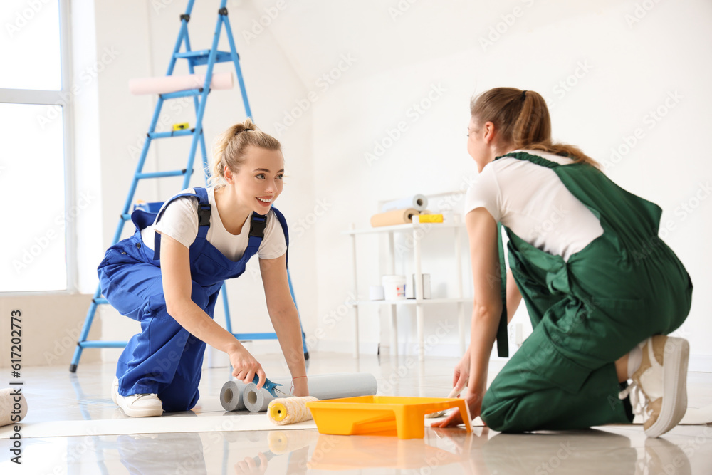 Female decorators gluing wallpaper in room