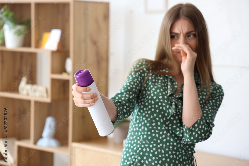 Displeased young woman with air freshener at home