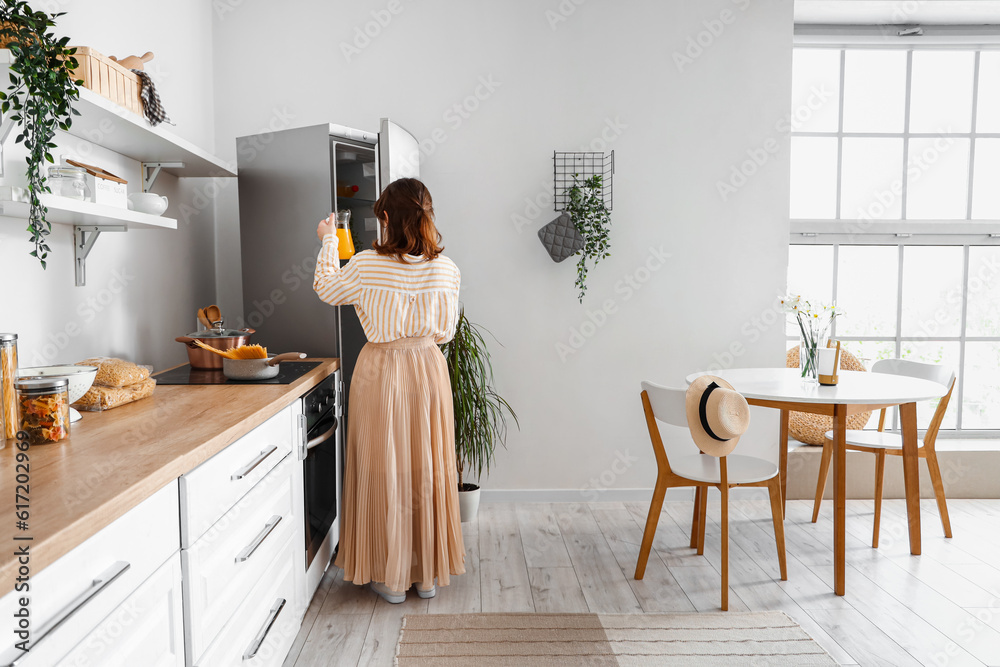 Young woman opening stylish fridge in kitchen