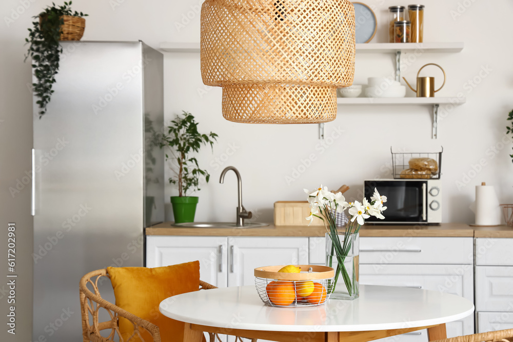 Interior of light kitchen with stylish fridge, counters, lamp and table