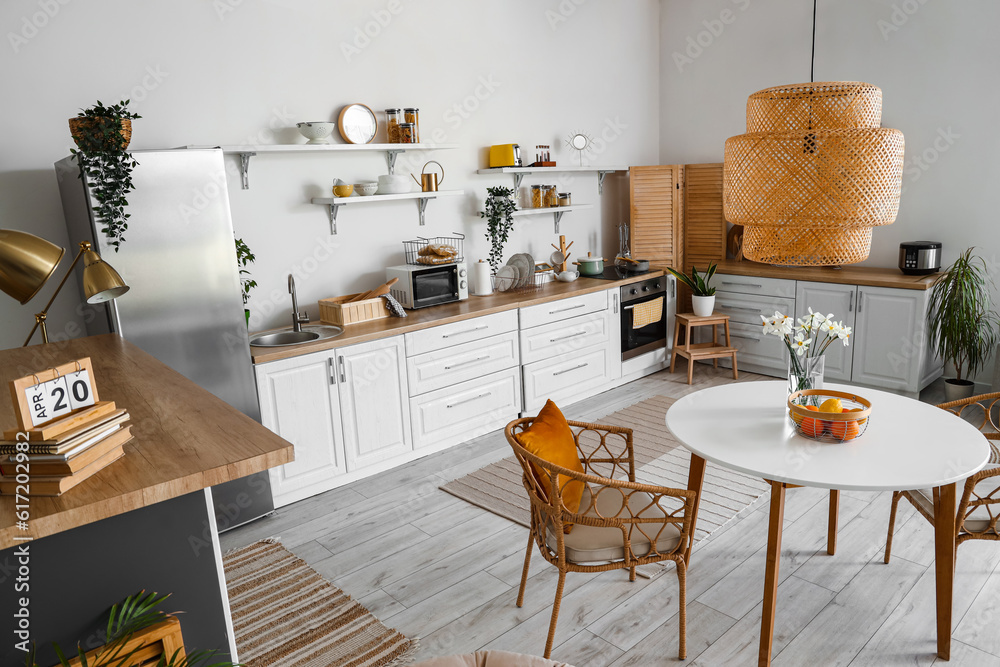 Interior of light kitchen with stylish fridge, counters, lamp, table and chairs