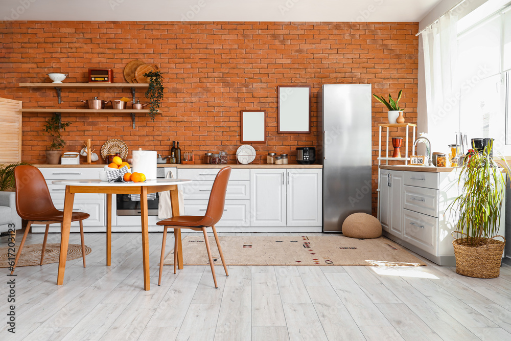 Interior of kitchen with stylish fridge, counters, shelves, table and blank pictures