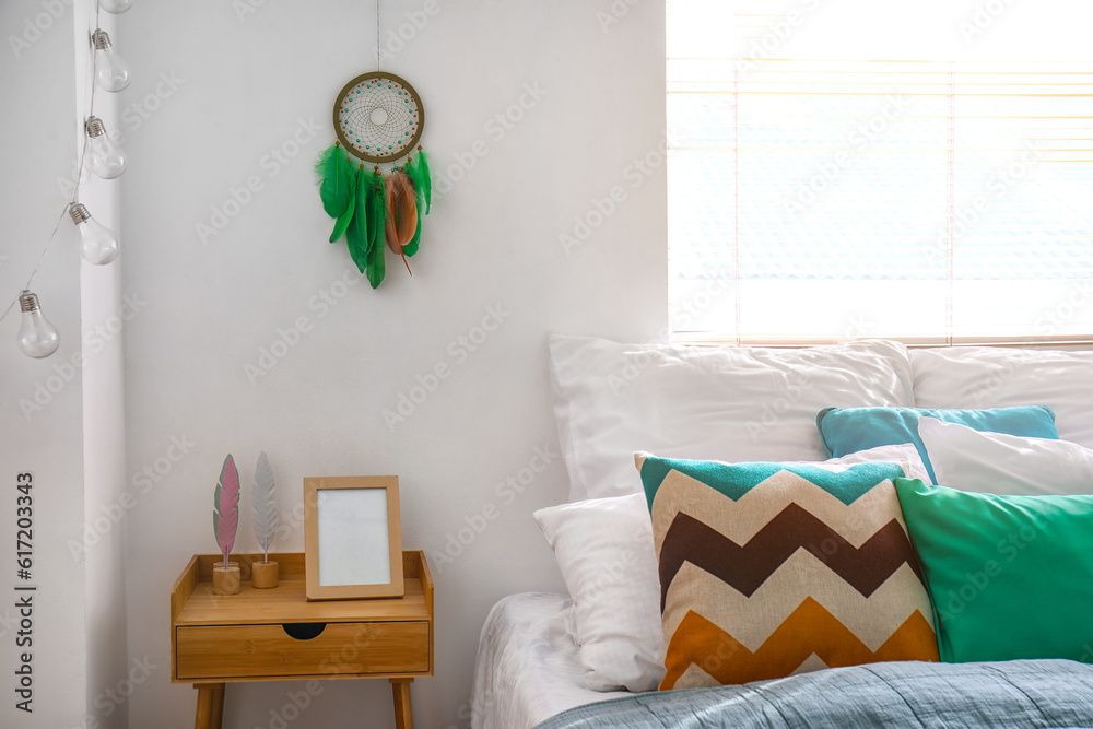 Interior of modern bedroom with bed, bedside table and dream catcher hanging on white wall