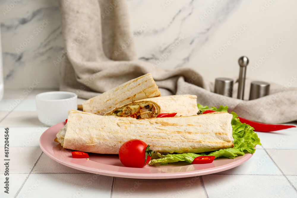 Plate of tasty shawarma with lettuce and tomatoes on white tile table