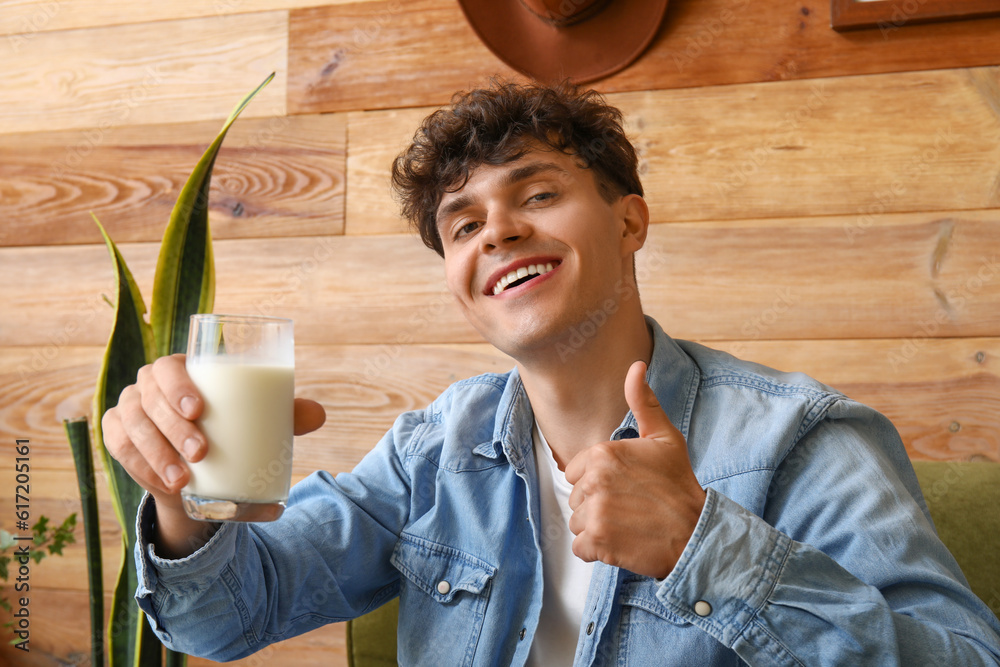 Young man with glass of milk showing thumb-up at home