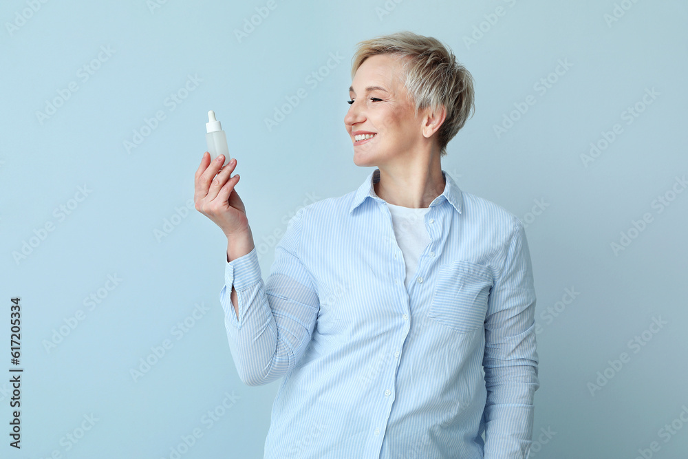 Mature woman with bottle of serum on light background