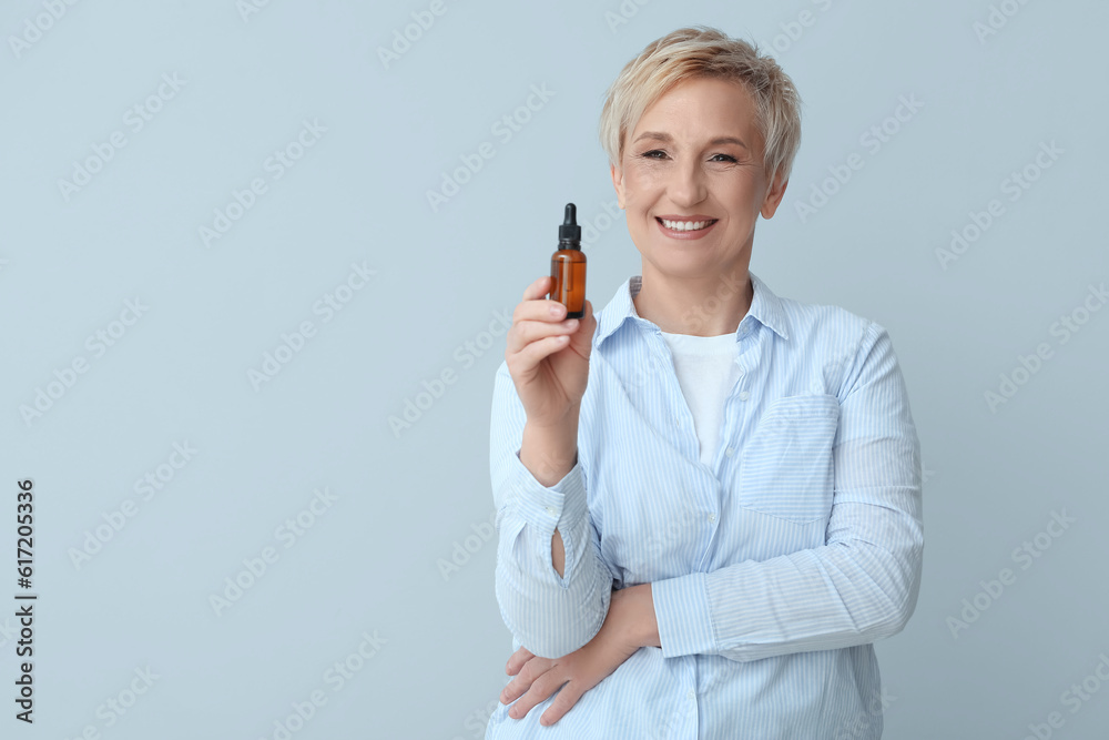 Mature woman with bottle of serum on light background