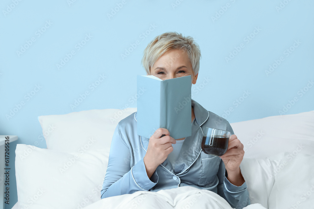 Mature woman with cup of coffee and notebook in bed