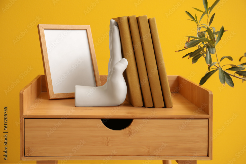 Stylish bookend and blank frame on table near yellow wall