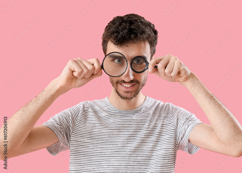 Young man with magnifiers on pink background