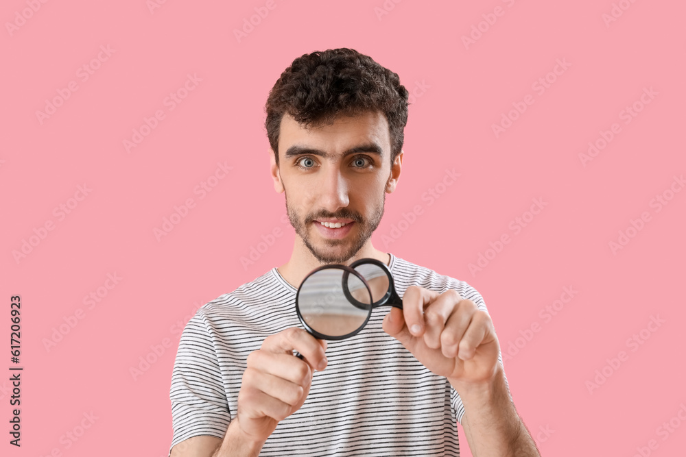 Young man with magnifiers on pink background