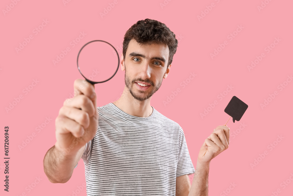 Young man with magnifier and speech bubble on pink background