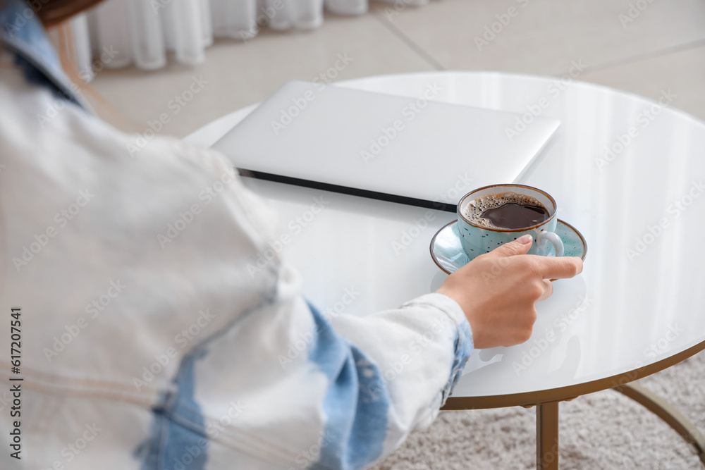 Woman taking cup of coffee from table with modern laptop