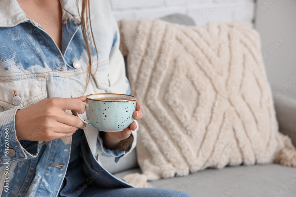 Woman sitting on sofa and holding cup of delicious coffee