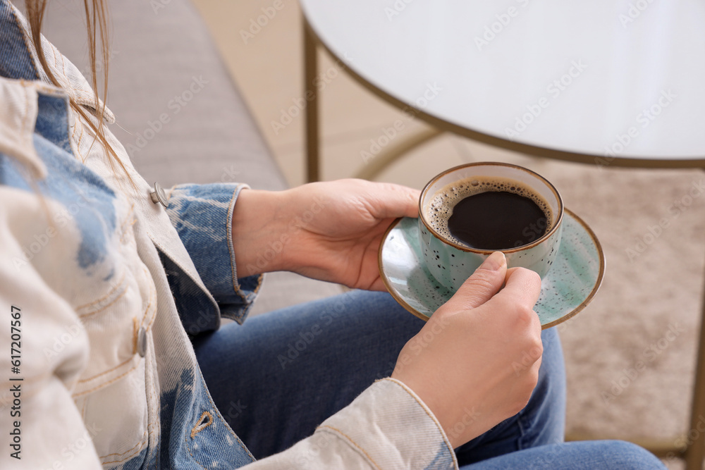 Woman sitting on sofa and holding cup of delicious coffee