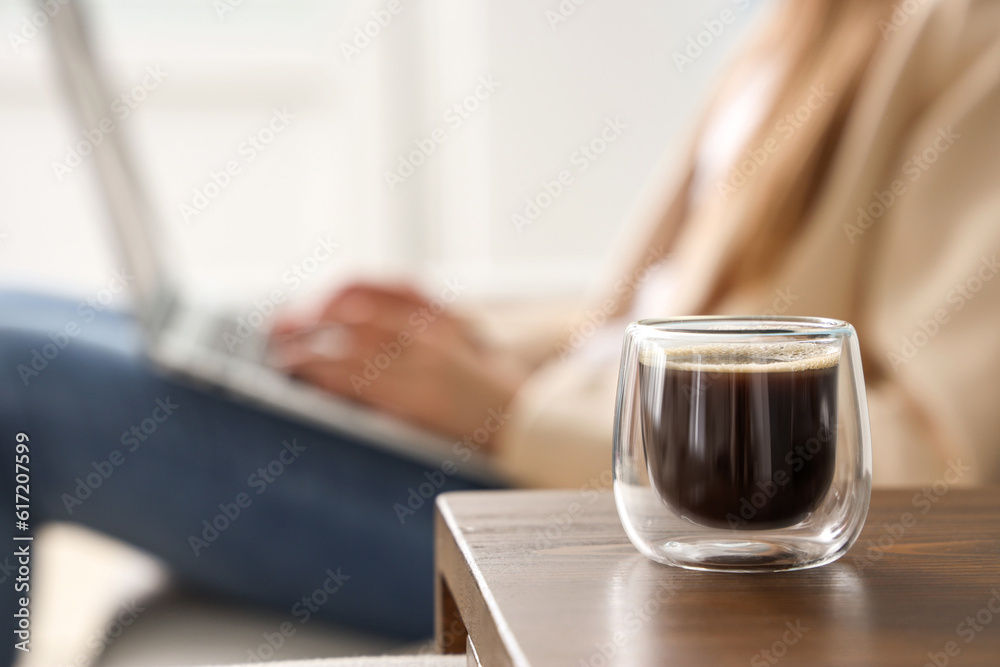 Woman sitting on sofa and using laptop near table with glass of delicious coffee