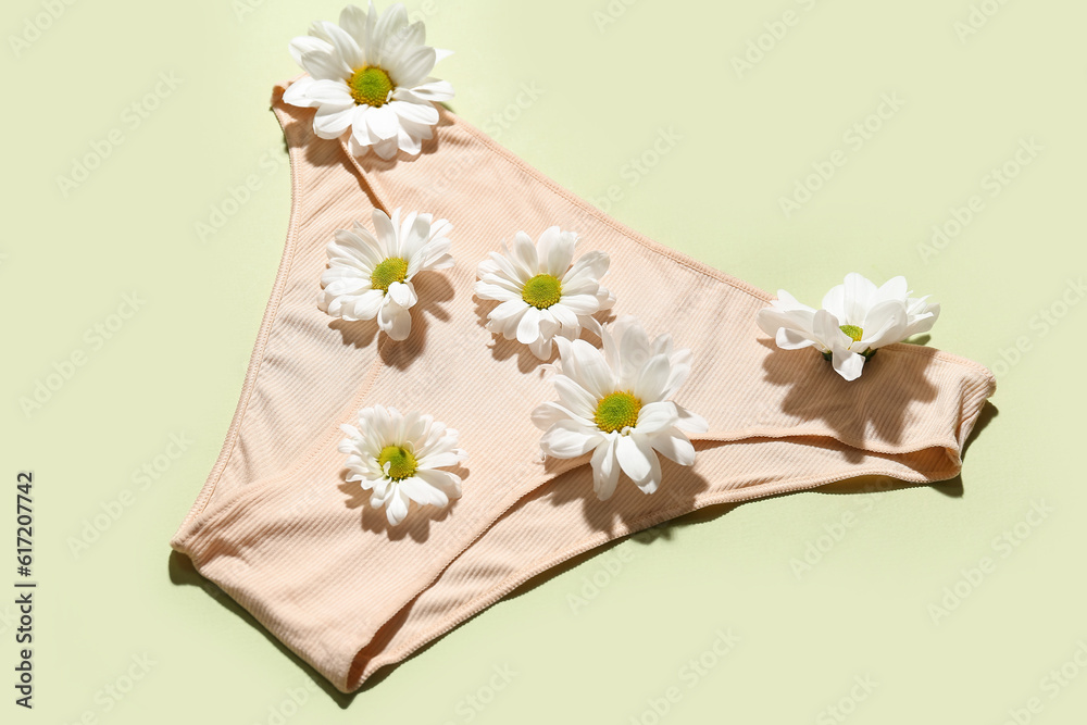 Composition with female panties and beautiful chamomile flowers on green background