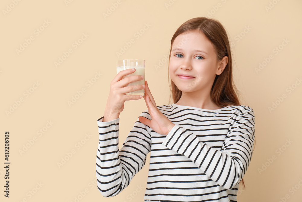 Little girl with glass of milk on beige background