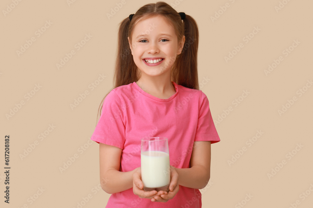 Little girl with glass of milk on beige background