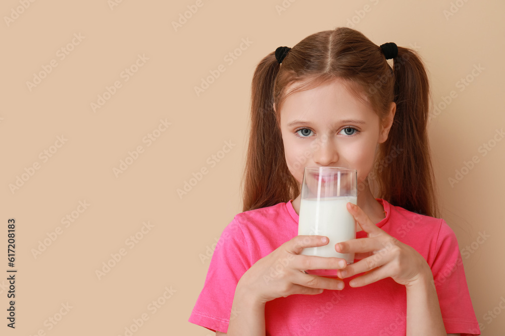 Little girl with glass of milk on beige background