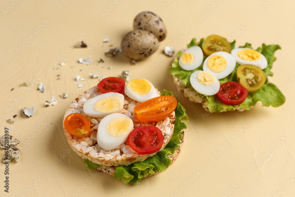 Rice crackers with quail eggs, tomatoes and lettuce on beige background, closeup