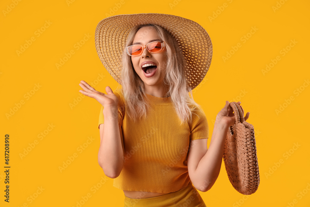 Happy young woman in stylish sunglasses with bag on orange background