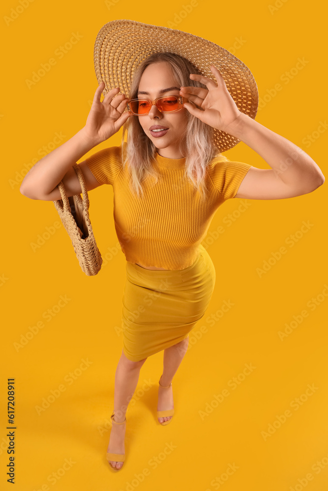 Young woman in stylish sunglasses with bag on orange background