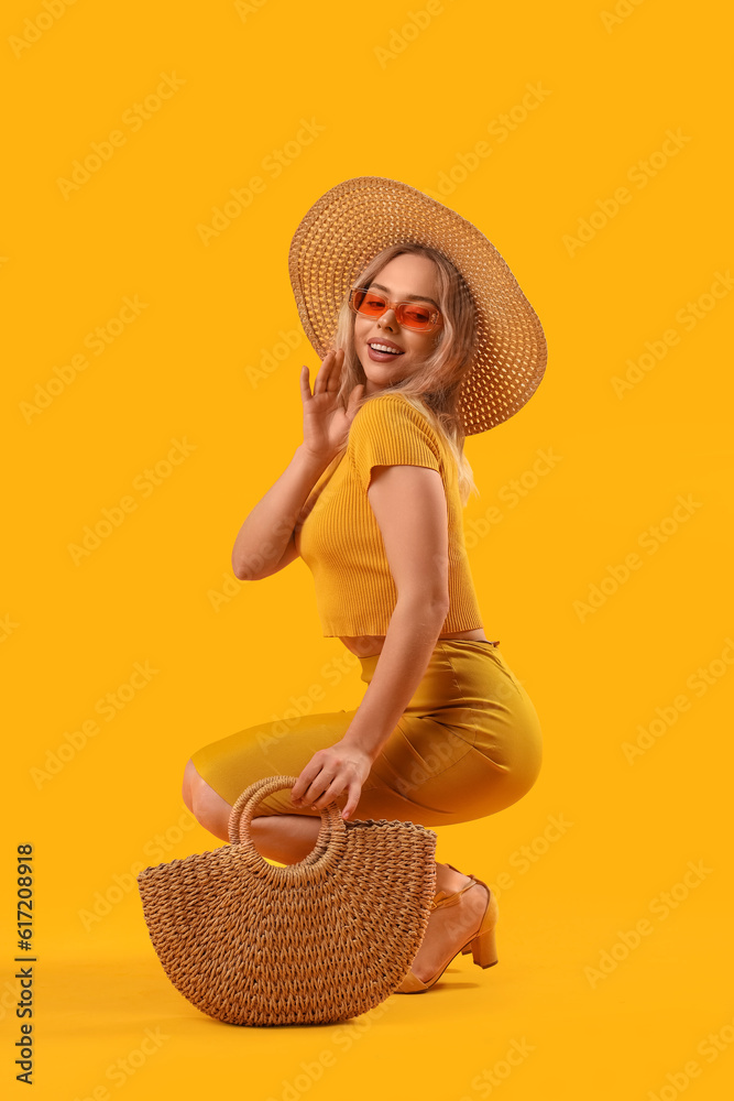 Young woman in stylish sunglasses with bag on orange background