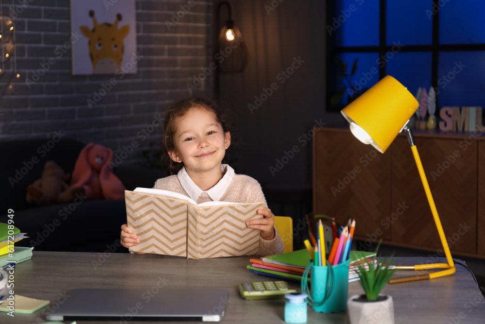 Little girl reading book at home late in evening