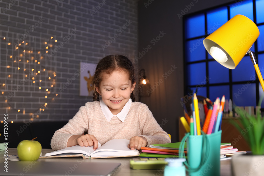 Little girl reading book at home late in evening