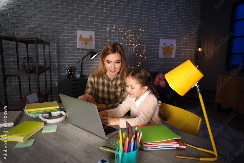 Little girl with her mother doing lessons at home late in evening