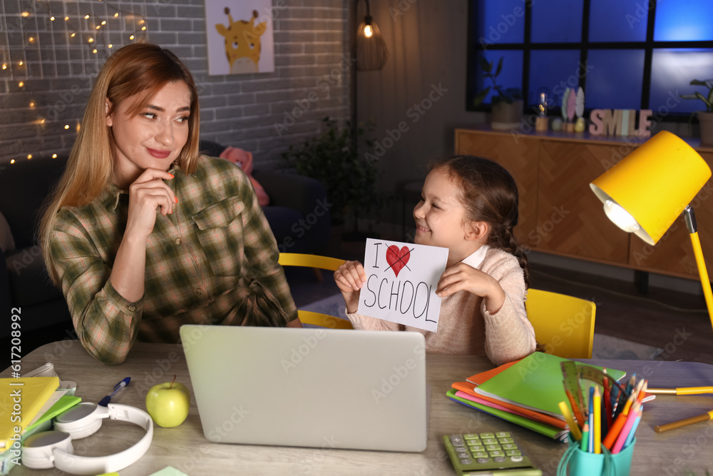 Little girl holding paper with text I DONT LOVE SCHOOL and her mother at home late in evening