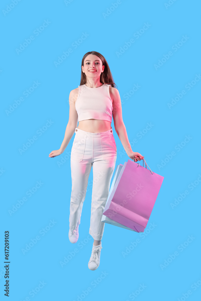 Young woman with shopping bags jumping on blue background