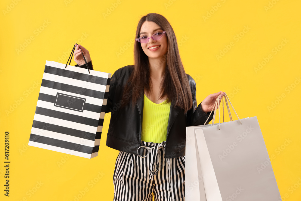 Young woman with shopping bags on yellow background